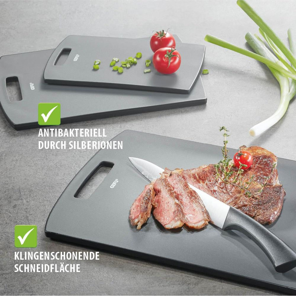 Ein Steak wird auf einem Schneidebrett geschnitten, daneben Tomaten und Zwiebeln.