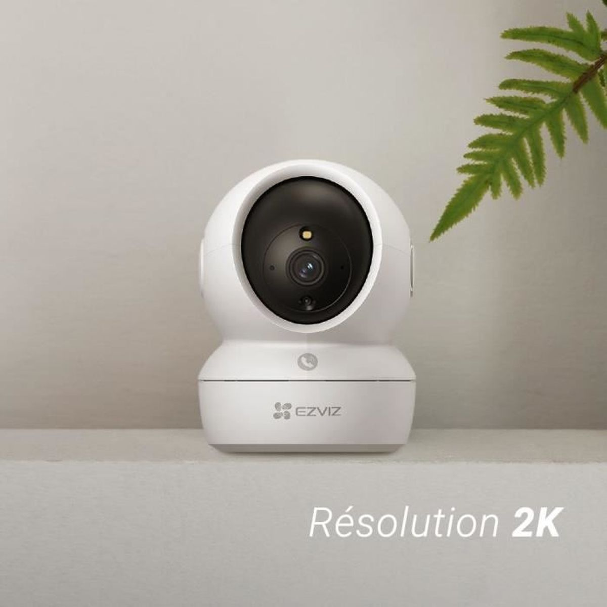 Biała kamera EZVIZ z czarnym obiektywem stoi na półce. Po prawej roślina.