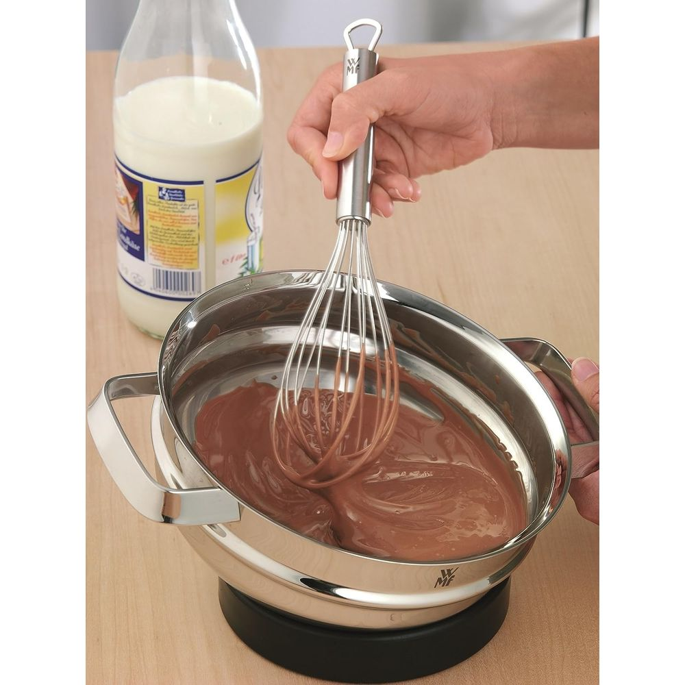 Trzepaczka miesza brązową czekoladę w metalowej misce, obok butelki mleka.