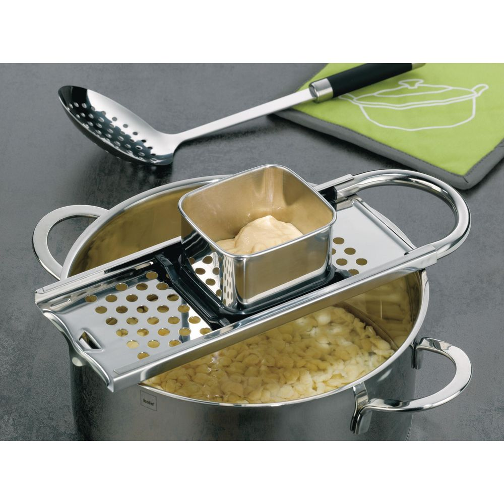 Un fabricant de spaetzle sur une casserole de spaetzle, avec une louche à proximité.