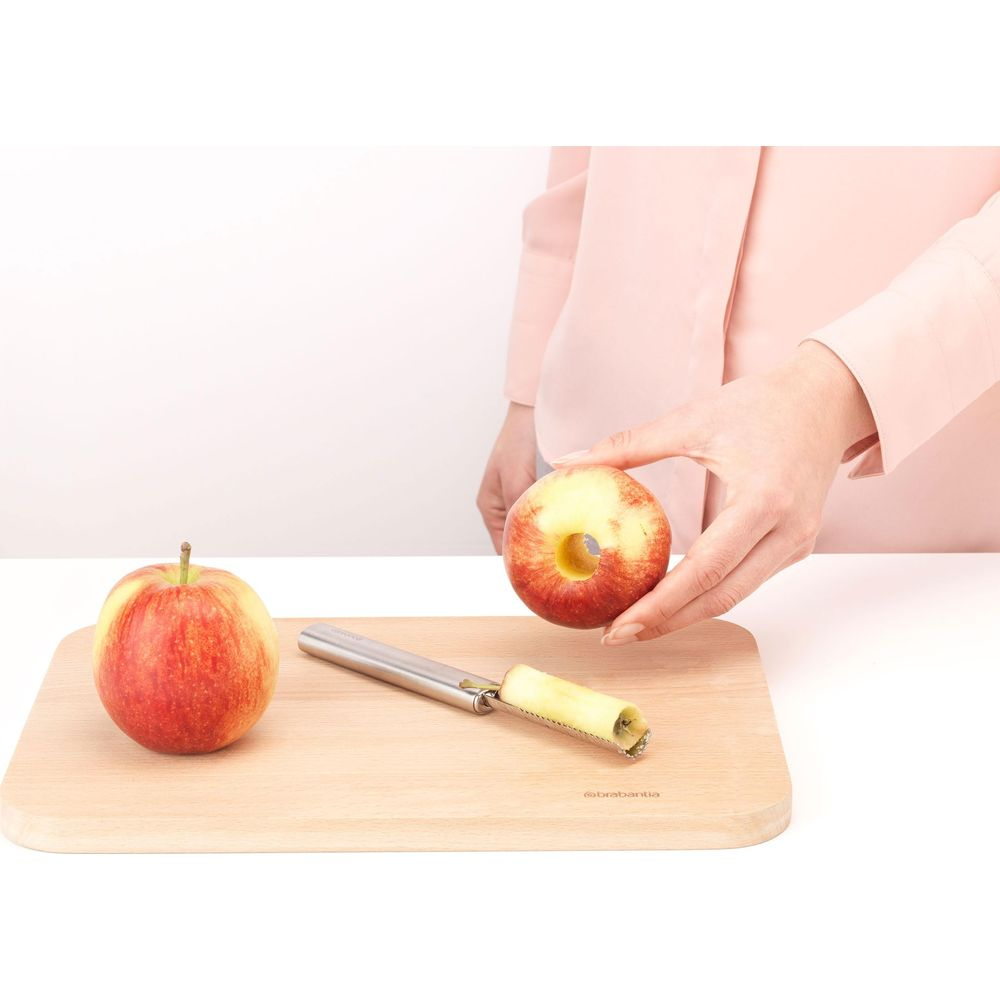 Eine Person entkernt einen Apfel auf einem Holzschneidebrett mit einem Entkerner.