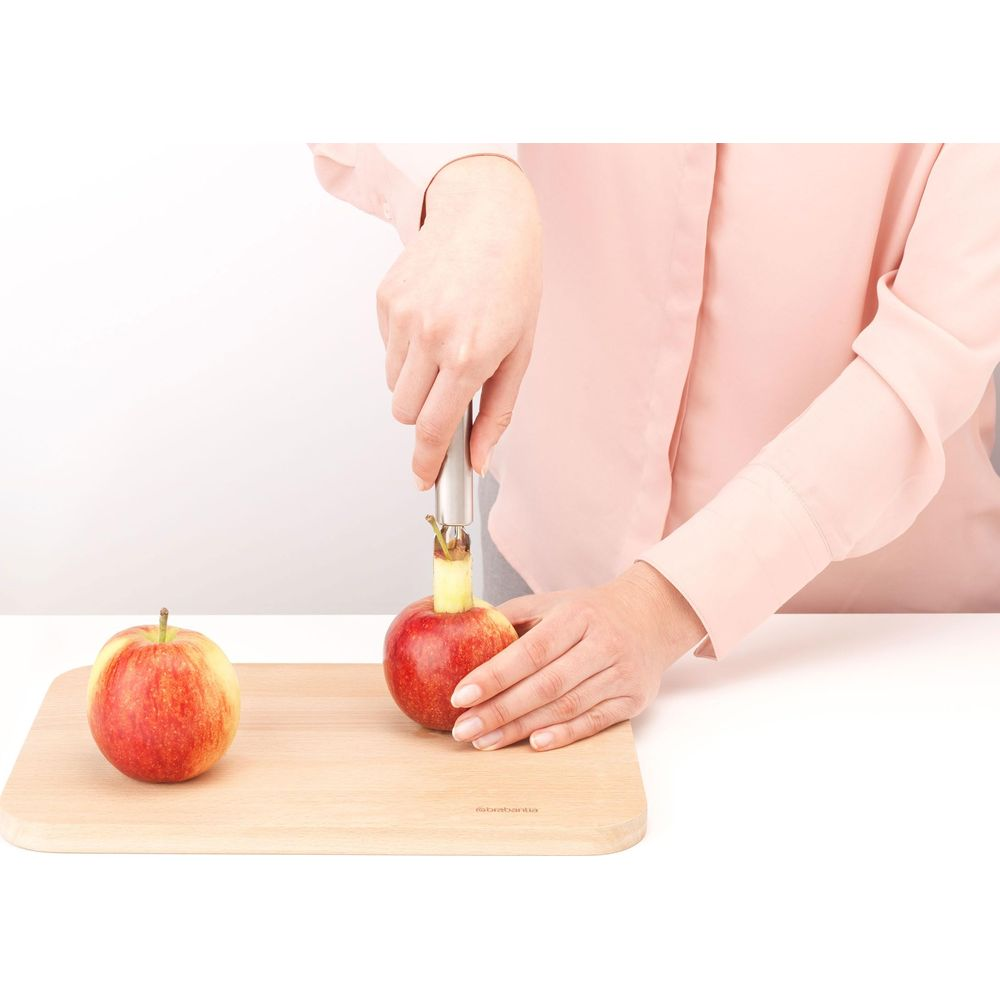 Person entkernt einen Apfel auf einem Holzbrett mit einem Entkerner.
