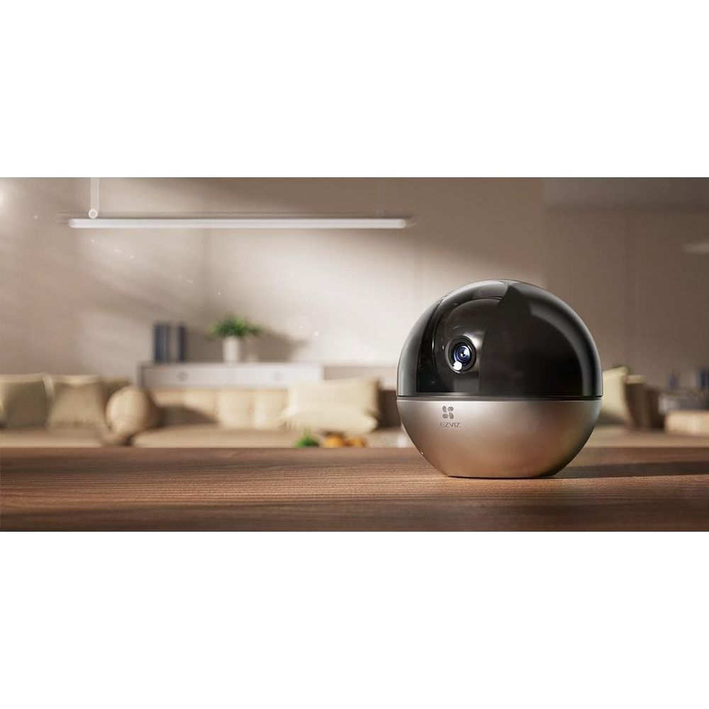 Sferyczna kamera bezpieczeństwa z srebrną podstawą i czarną kopułą stoi na drewnianym stole.