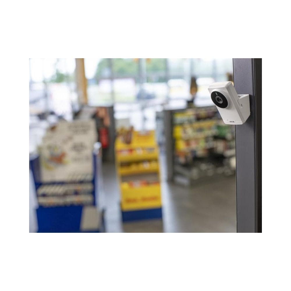 Biała kamera zamontowana na ciemnym słupie, za nią sklep z półkami.