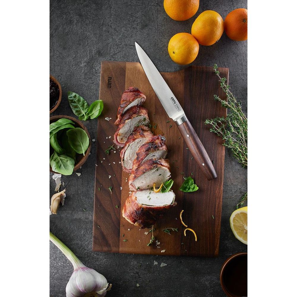 Bacon-umwickeltes Hähnchen auf Holzbrett mit Messer, Orangen, Knoblauch und Kräutern.