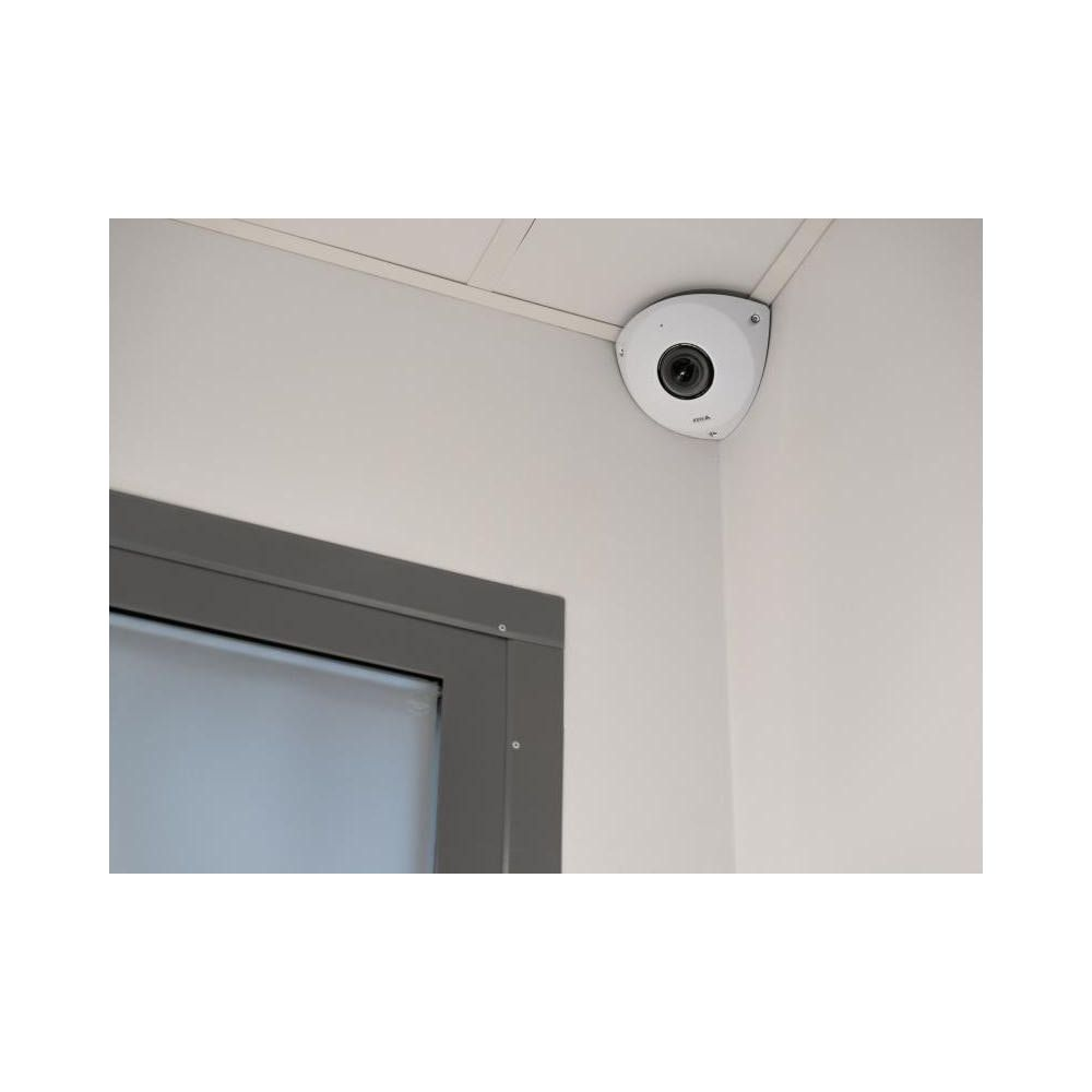 Biała kamera monitorująca zamontowana na białej ścianie w rogu, nad szarymi drzwiami.
