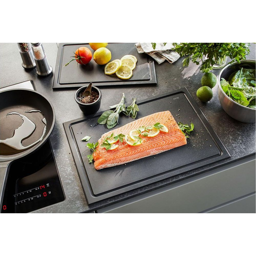 Roher Lachs auf schwarzem Brett mit Zitronenscheiben, Kräutern, Tomaten, Limetten, Spinat.