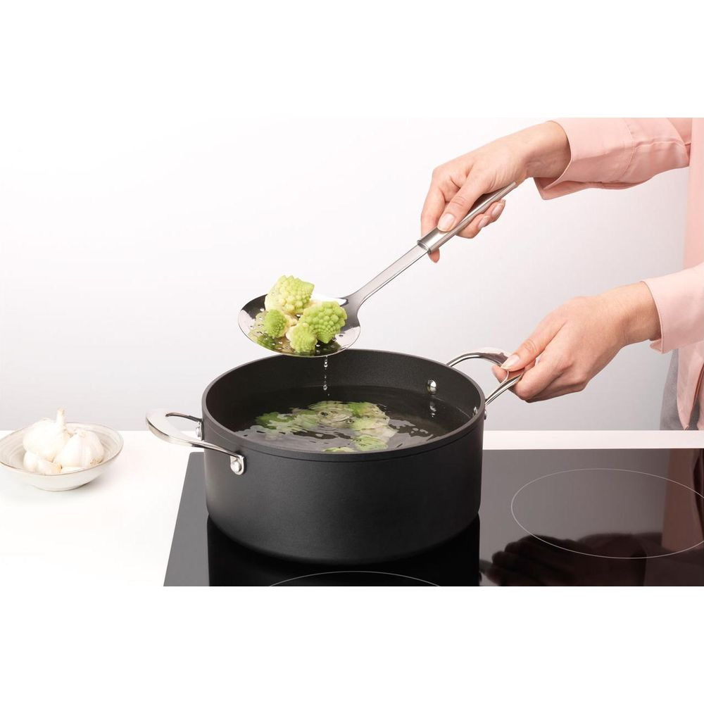 Verdure verdi sollevate dall'acqua bollente con schiumarola.
