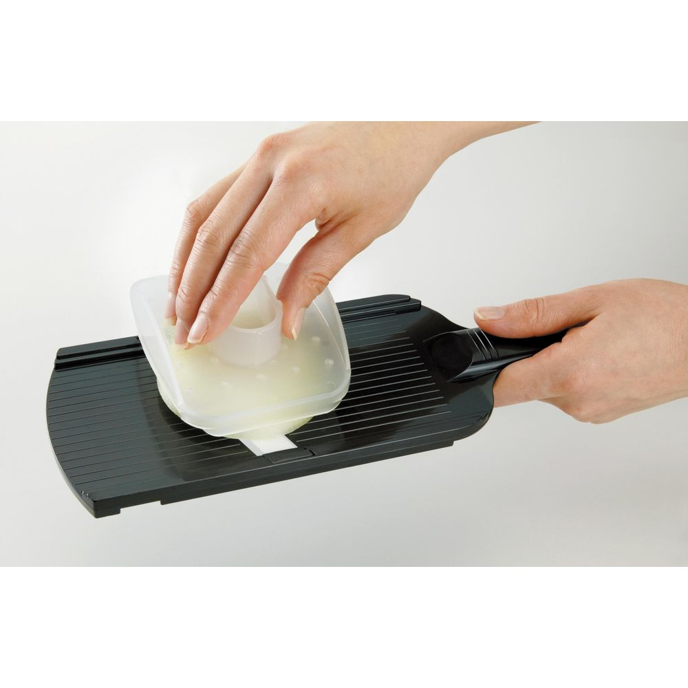 Eine Hand hält einen transparenten Behälter mit Zwiebeln auf einem schwarzen Hobel.