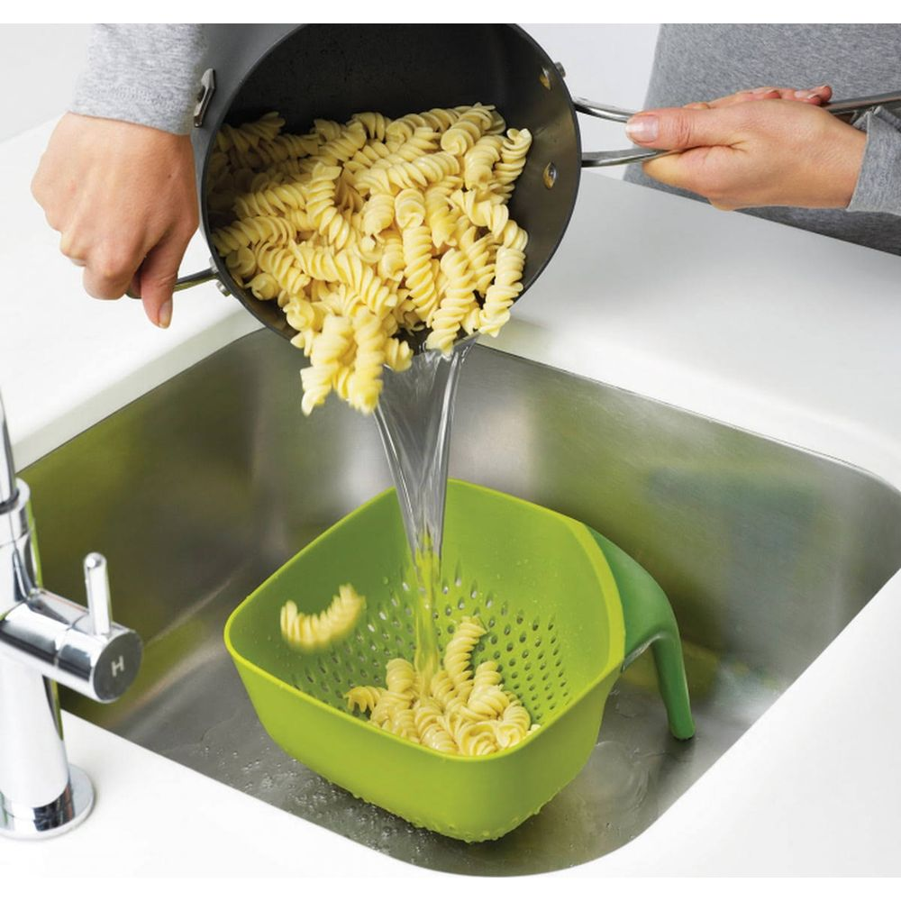 La pasta cocida se vierte de una olla a un colador verde en un fregadero.