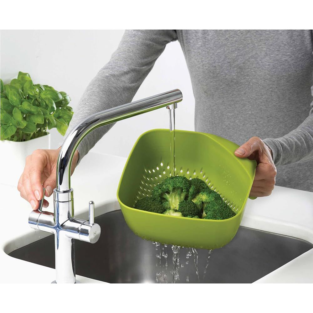 Brócoli siendo lavado en un colador verde bajo agua corriente en un fregadero.