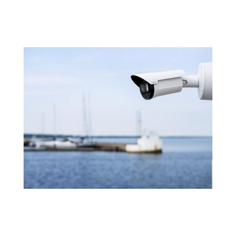 Biała kamera monitoringu nadzoruje spokojny port z łodziami w tle.