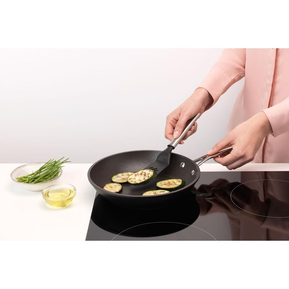 Zucchine fritte in padella, con erba cipollina e olio vicino.