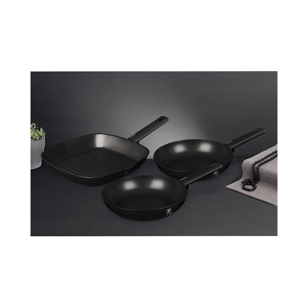 Drei schwarze Pfannen, eine Grillpfanne, auf dunklem Hintergrund.