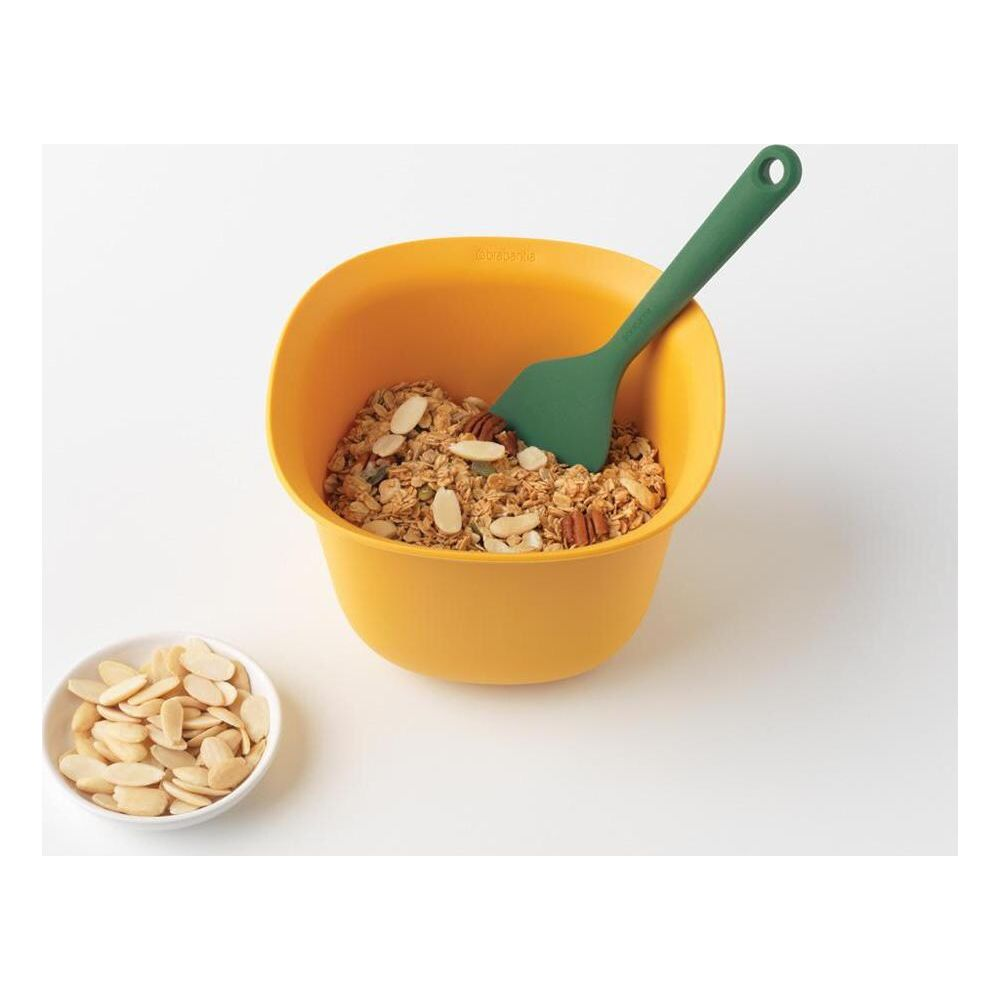 Żółta miska granoli z migdałami i orzechami pekan, z zieloną łopatką.