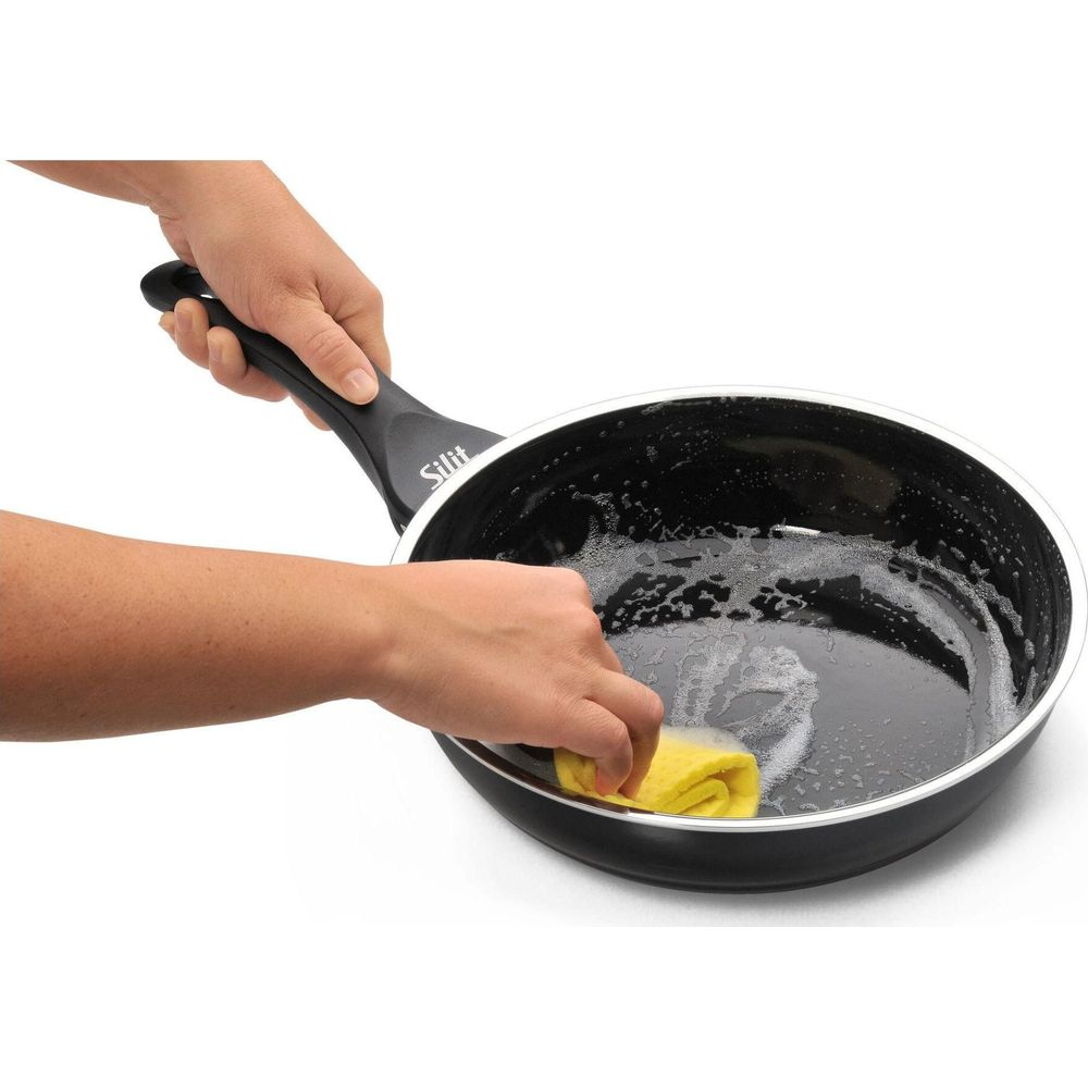Eine Hand reinigt eine schwarze Pfanne mit einem gelben Schwamm und Seifenlauge.