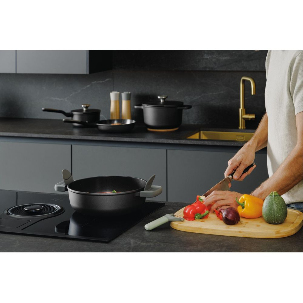 Man chopping bell peppers on a wooden board in a modern kitchen.