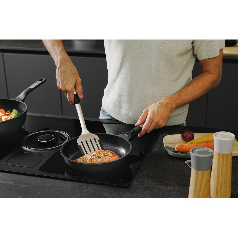 Man bakt zalm in pan op inductiekookplaat, met groenten ernaast.