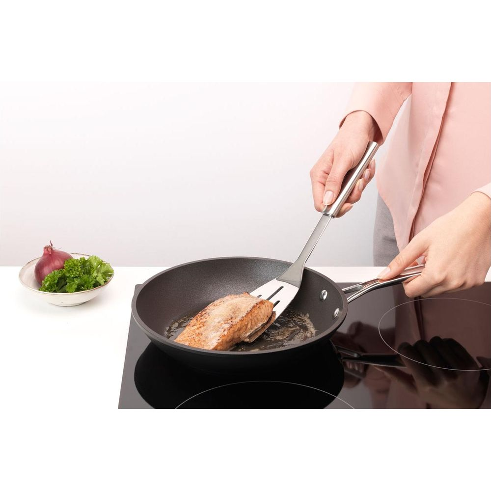 Filetto di salmone fritto in padella, accanto una ciotola con cipolla e prezzemolo.