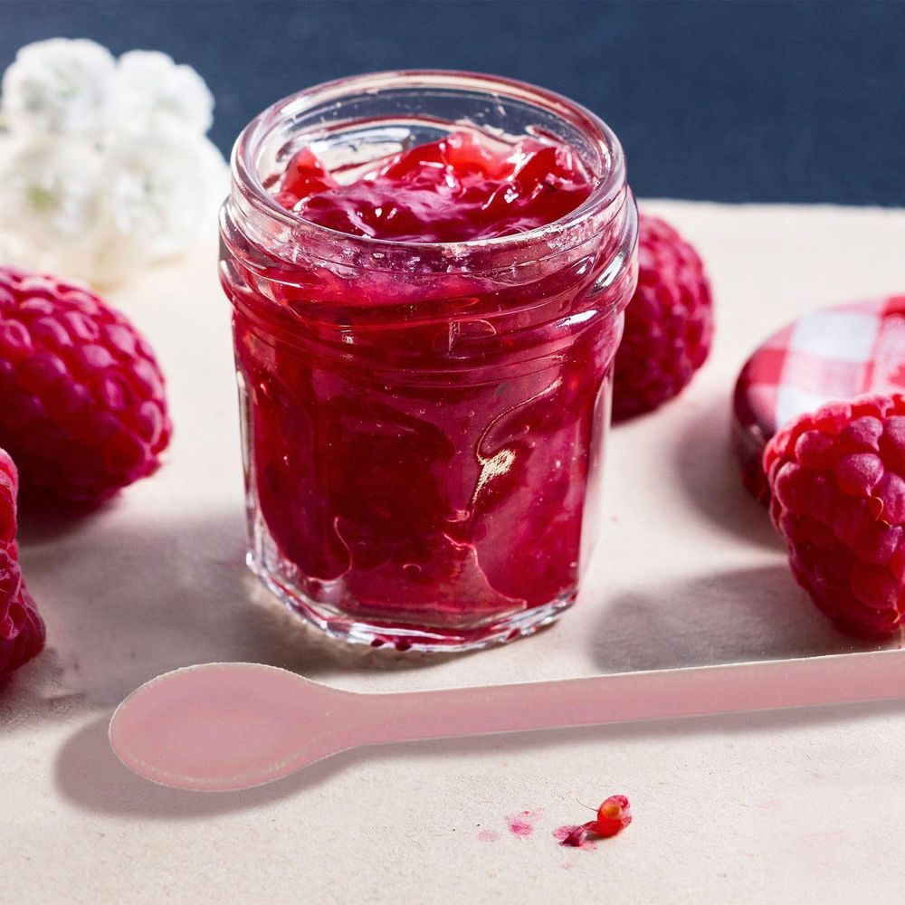 Un barattolo di marmellata di lamponi con lamponi freschi e un cucchiaino rosa.