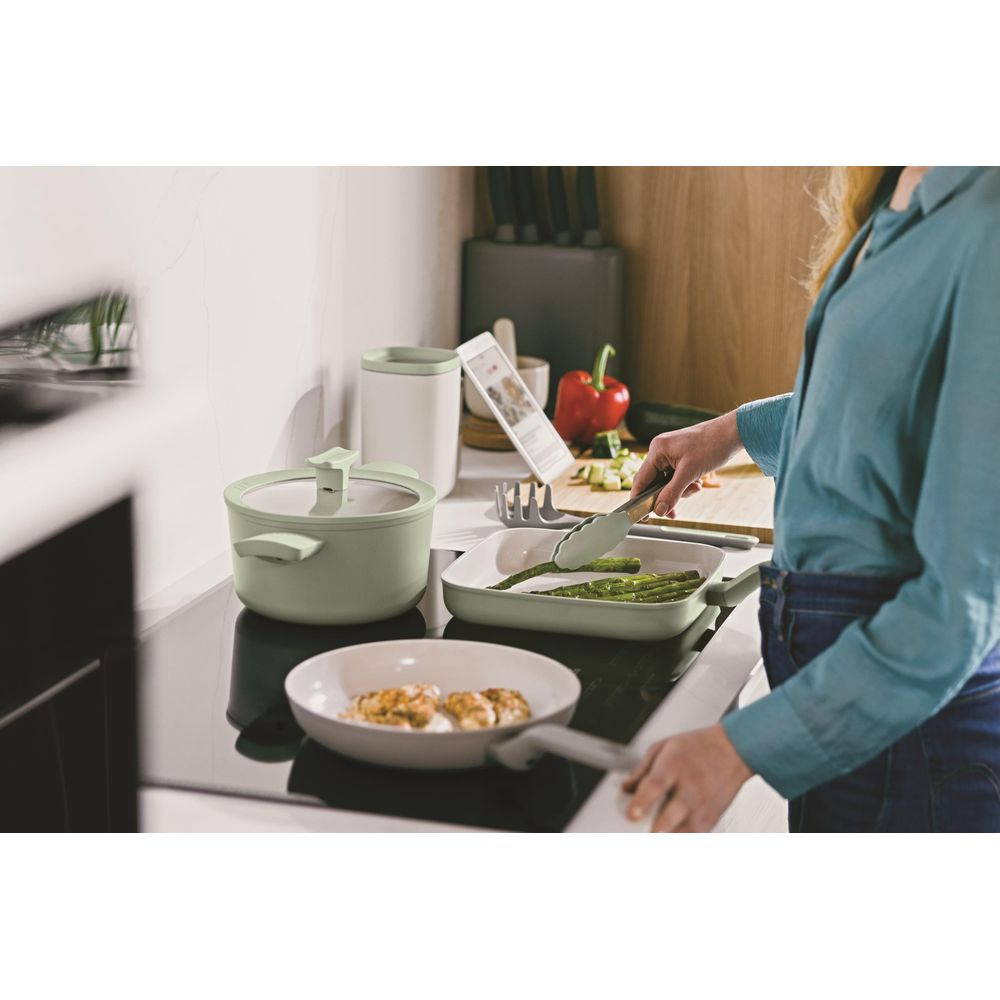 A person cooks asparagus and chicken in a kitchen on an induction stovetop.
