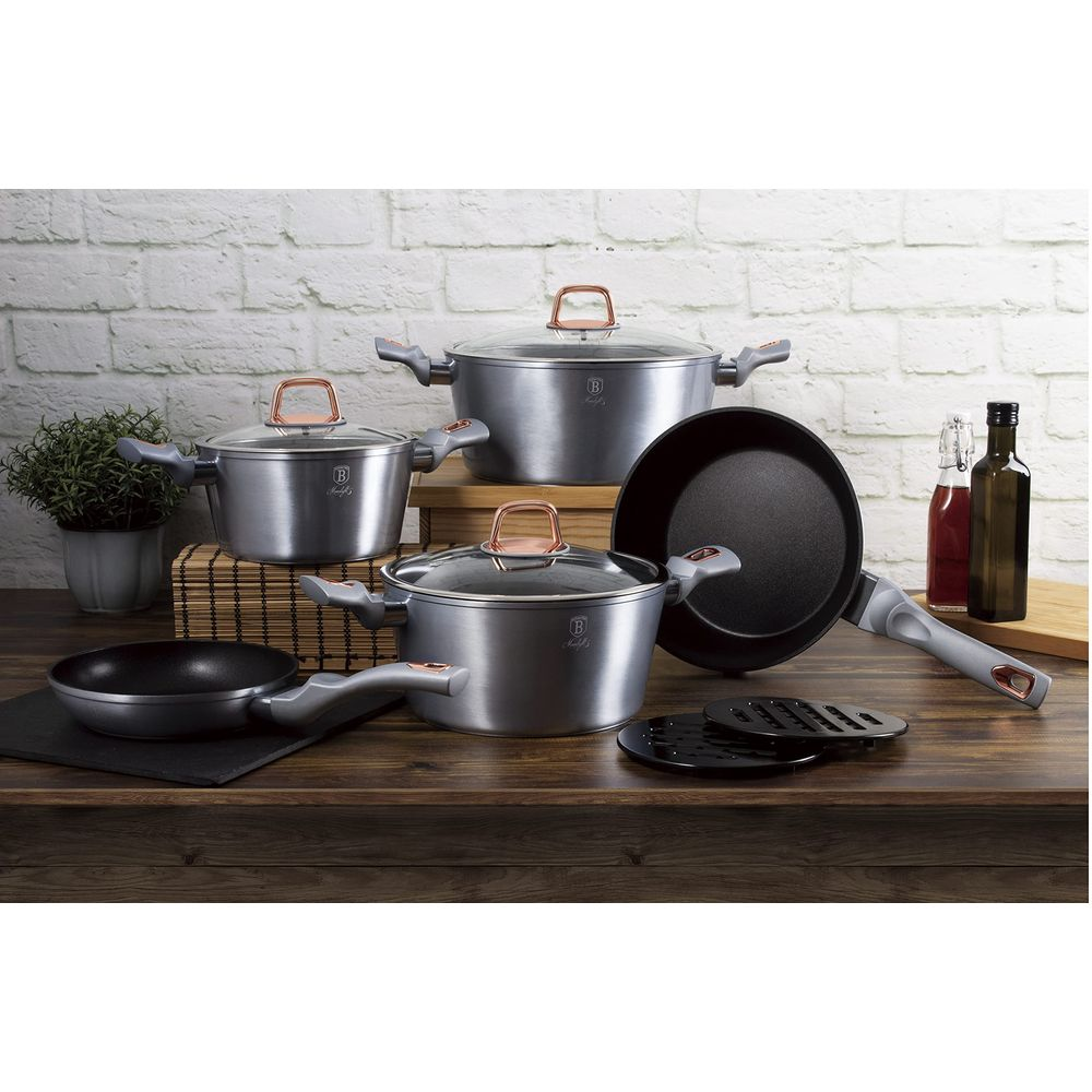 Juego de utensilios de cocina grises con tapas de vidrio y mangos de cobre sobre mesa.