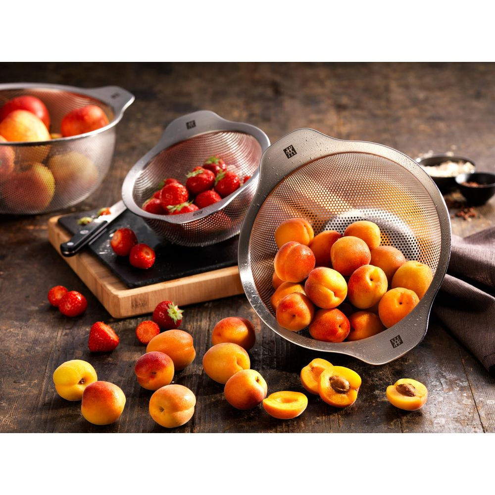Apricots and strawberries in strainers and scattered on a wooden table.
