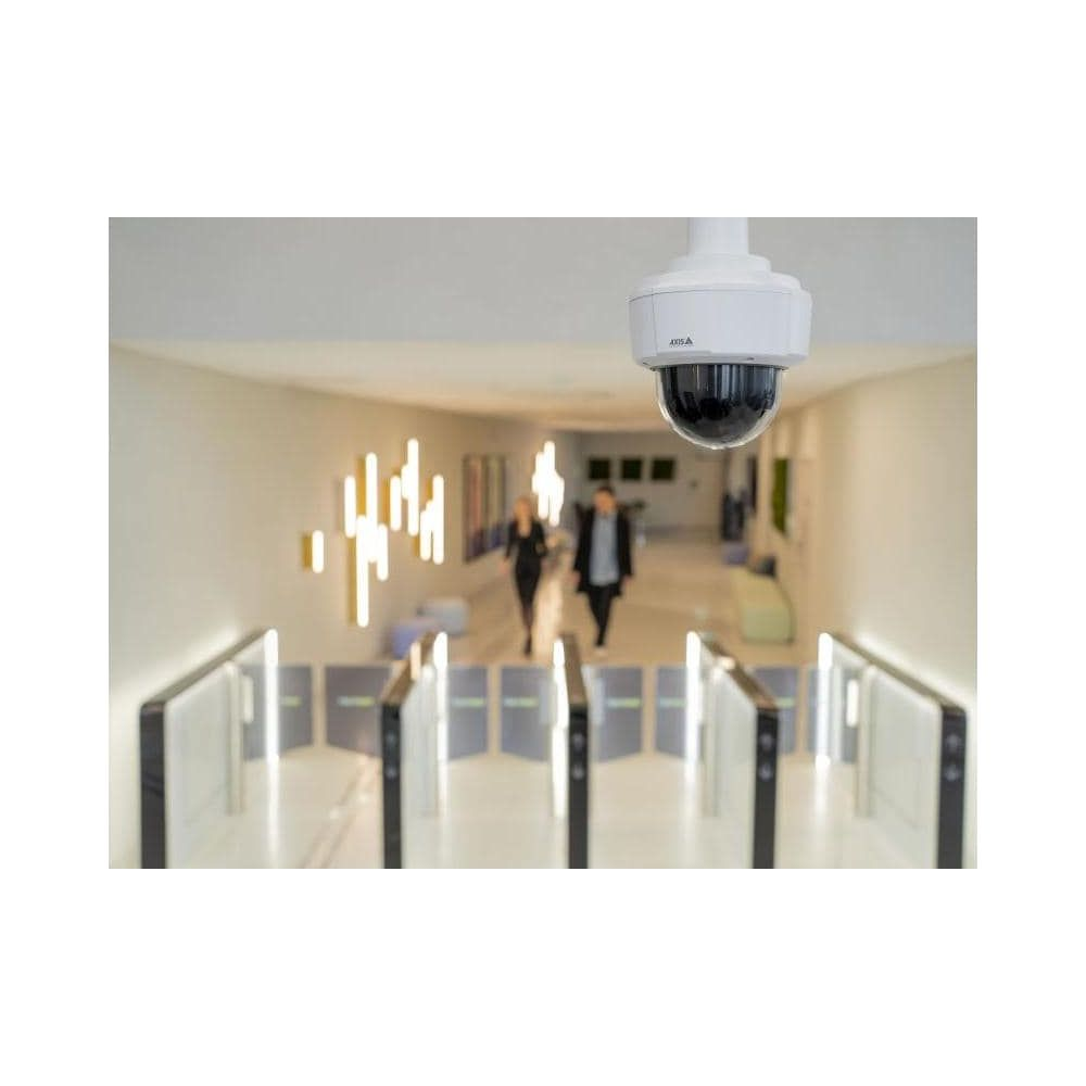 Kamera bezpieczeństwa nadzoruje hol z obrotowymi bramkami i dwiema idącymi osobami.