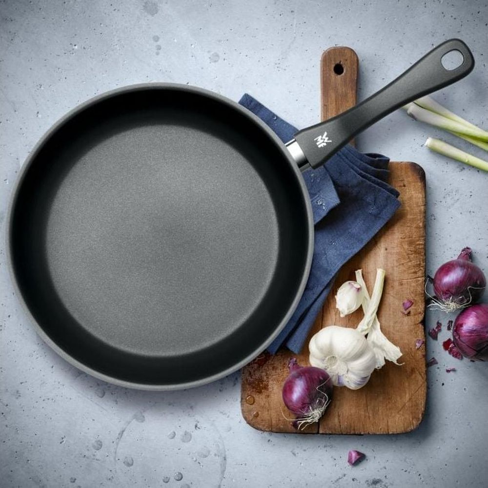 Szara patelnia z drewnianą deską, czosnkiem, cebulą i szczypiorkiem.