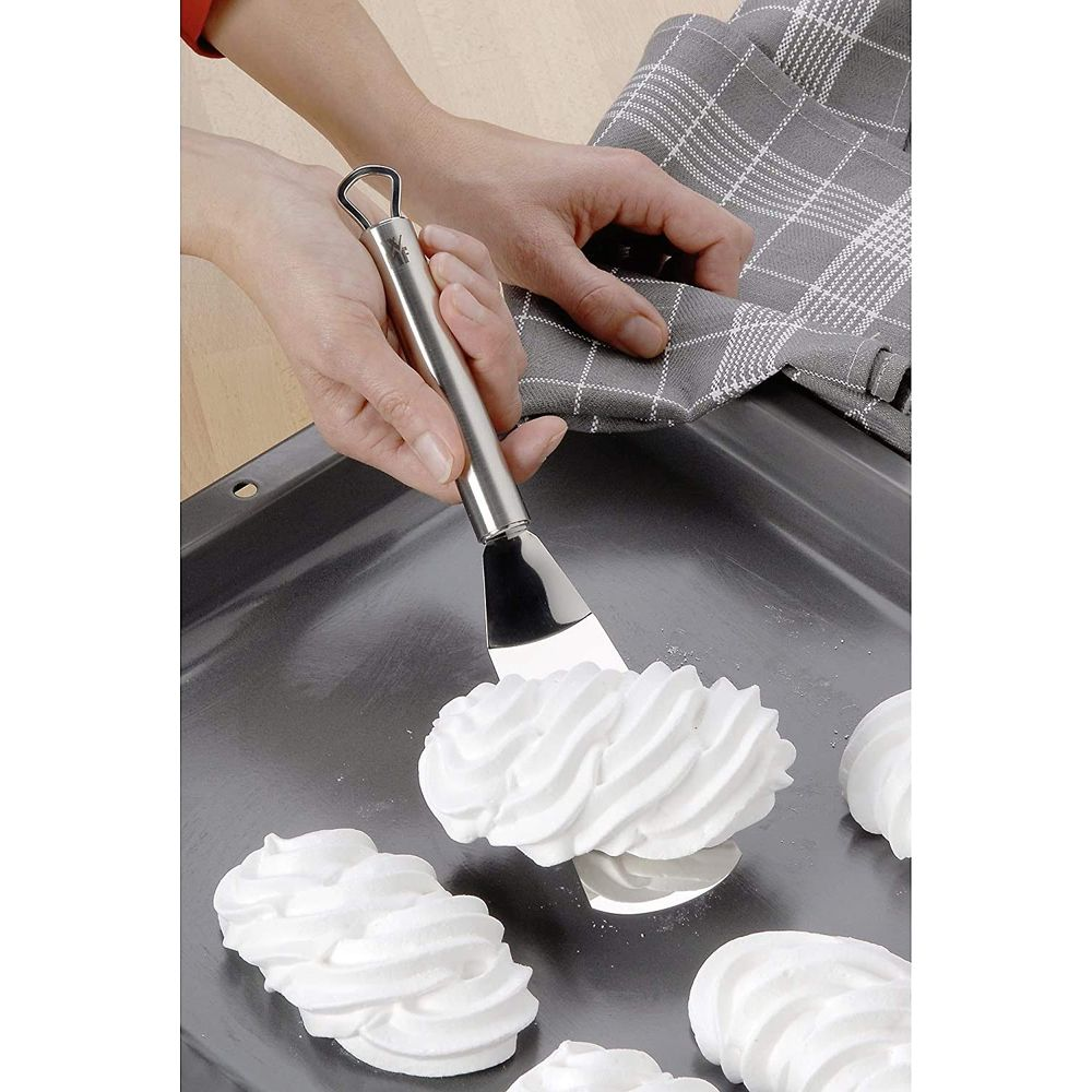 Ręka używa łopatki do przesuwania białych bez na blasze do pieczenia.