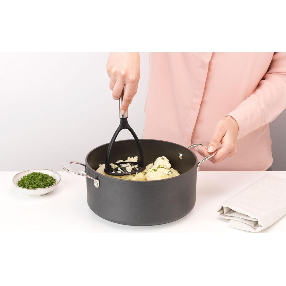 Eine Person zerdrückt Kartoffeln in einem Topf mit einem Kartoffelstampfer.