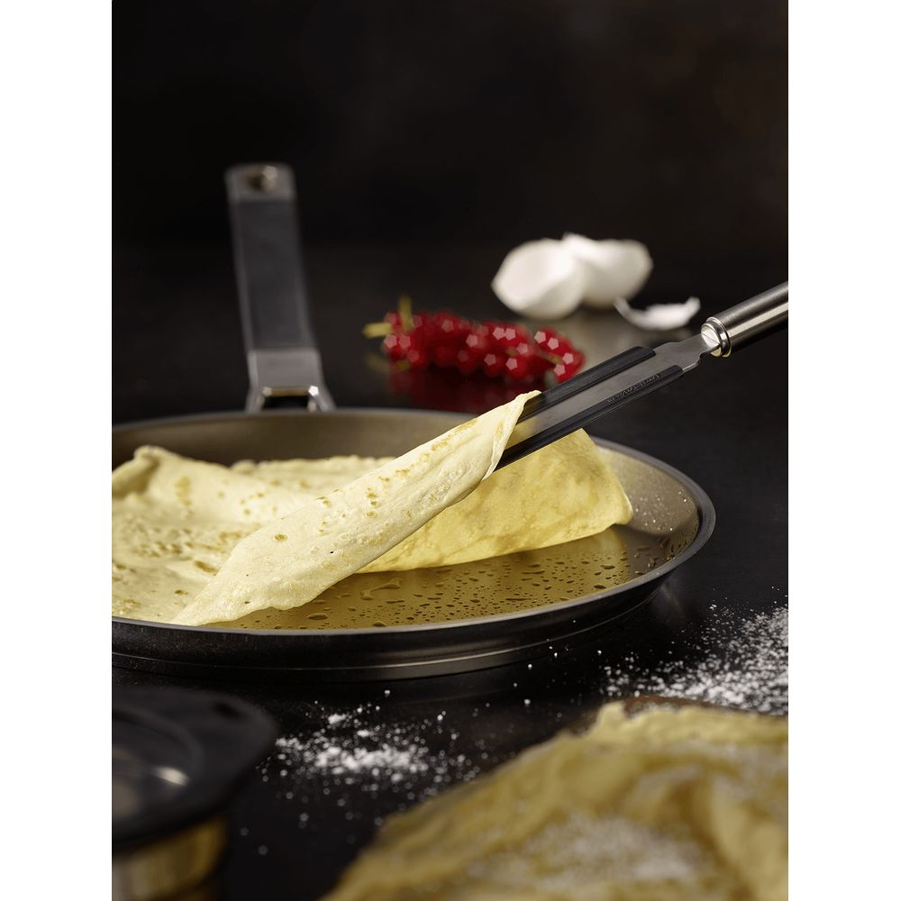 Ein Pfannkuchen wird mit einer Zange aus einer Pfanne gehoben.