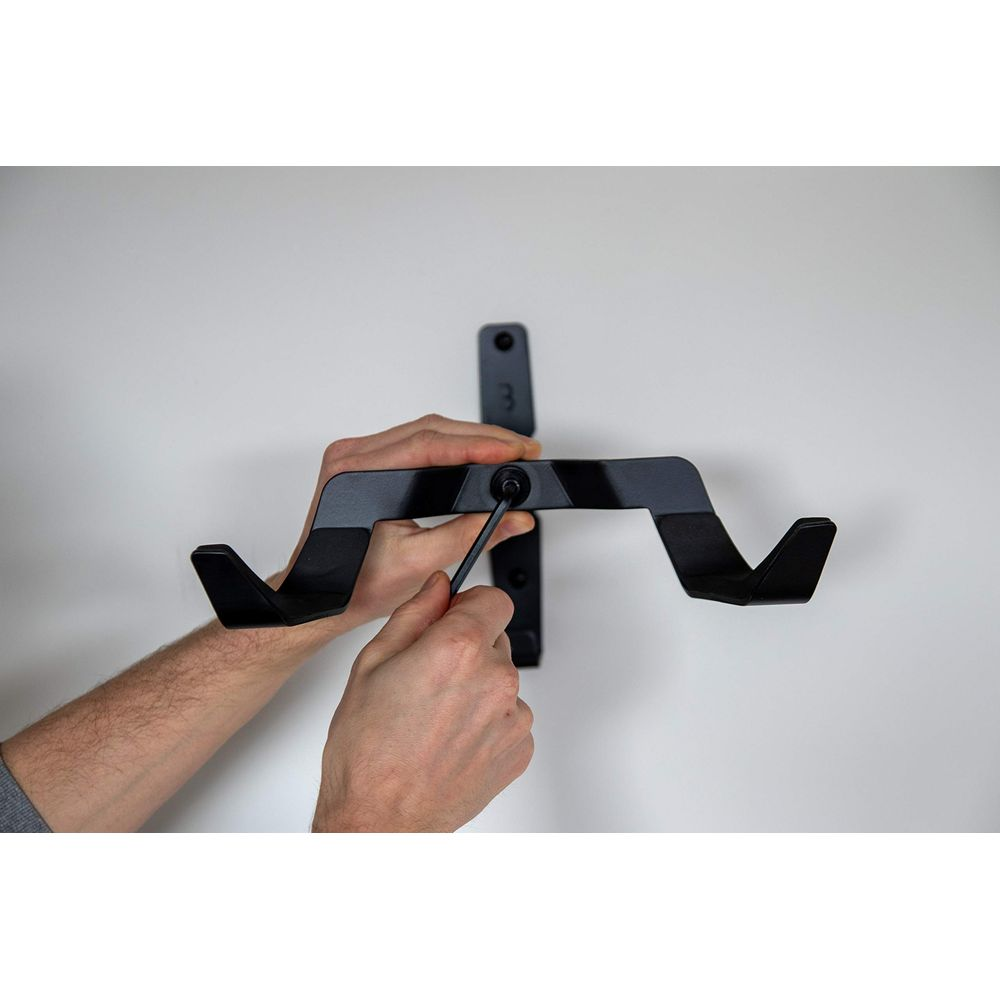 Osoba przykręca czarny uchwyt ścienny kluczem imbusowym.