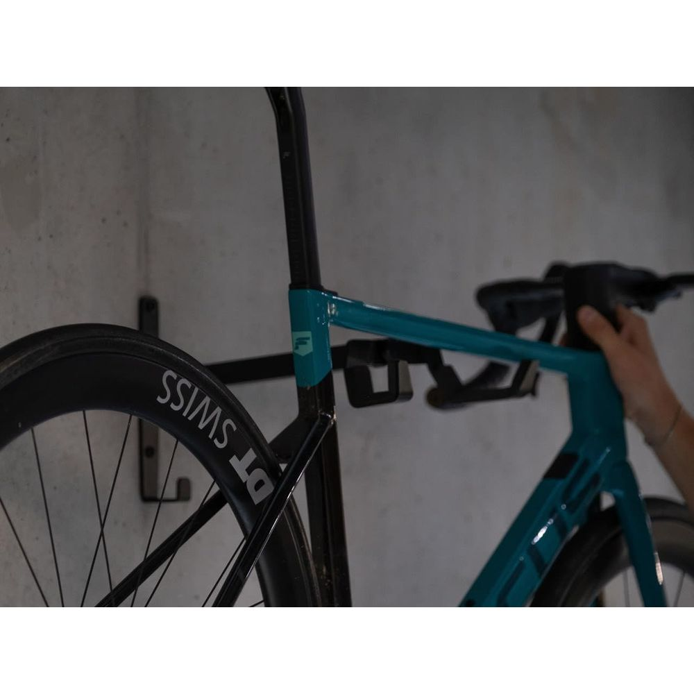 Niebiesko-zielony rower jest wieszany na uchwycie ściennym.