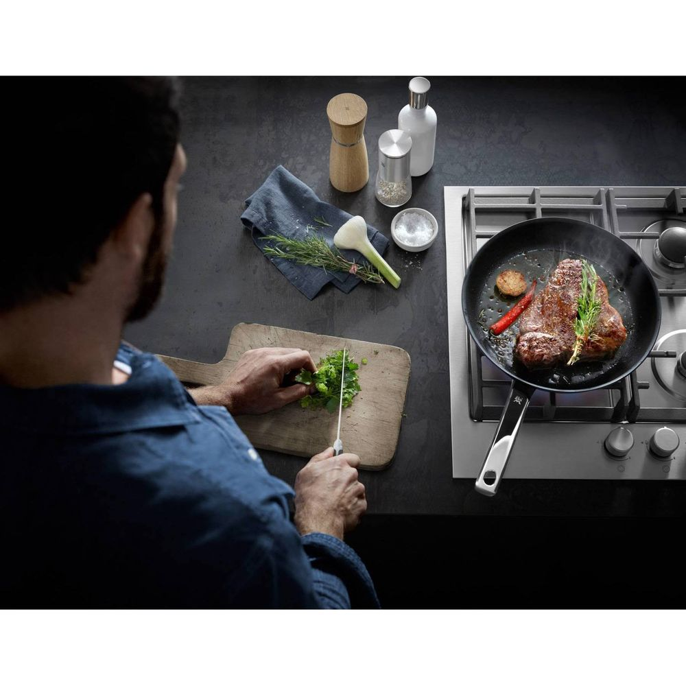 Mann schneidet Kräuter, während Steak in Pfanne brät.