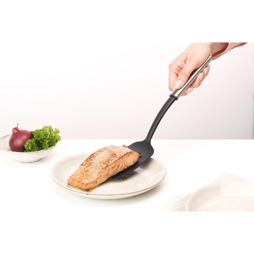 Un filetto di salmone viene posto su un piatto con una spatola nera.