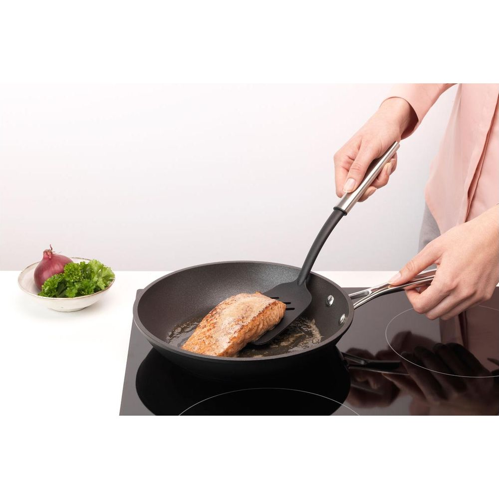 Un filetto di salmone viene fritto in padella, con una ciotola di cipolla e prezzemolo nelle vicinanze.