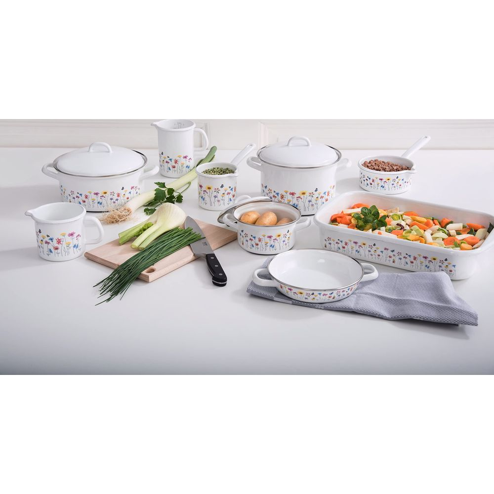 Ustensiles de cuisine blancs à motif floral, légumes et pommes de terre sur une table.