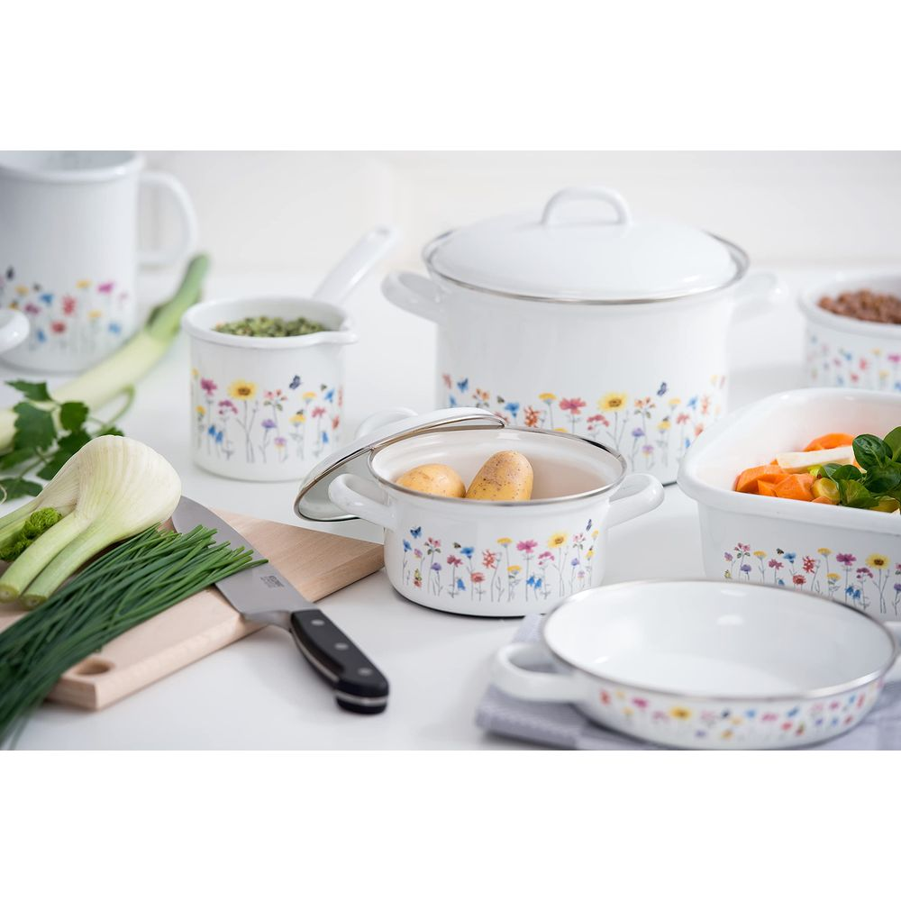 Ustensiles de cuisine en émail blanc à motif floral, sur une table avec des légumes.