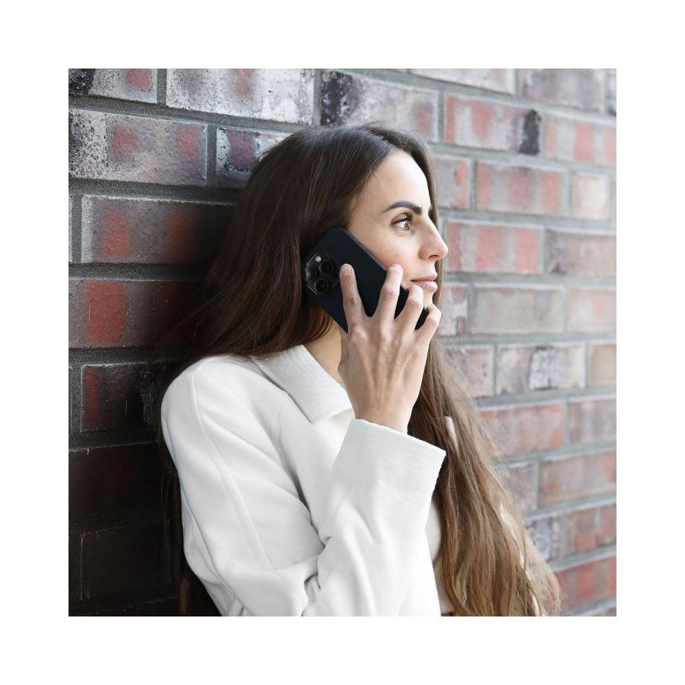 Frau mit langen braunen Haaren telefoniert mit einem schwarzen Handy vor einer Ziegelwand.