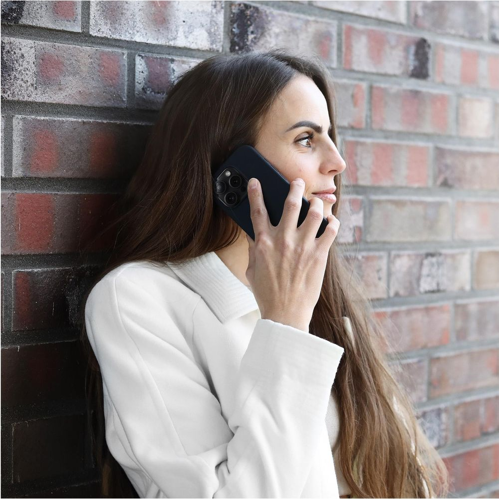 Une femme aux cheveux bruns s'appuie contre un mur de briques en parlant au téléphone.