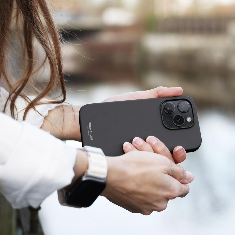 Una persona tiene un telefono nero con tre fotocamere. Un orologio è al polso.
