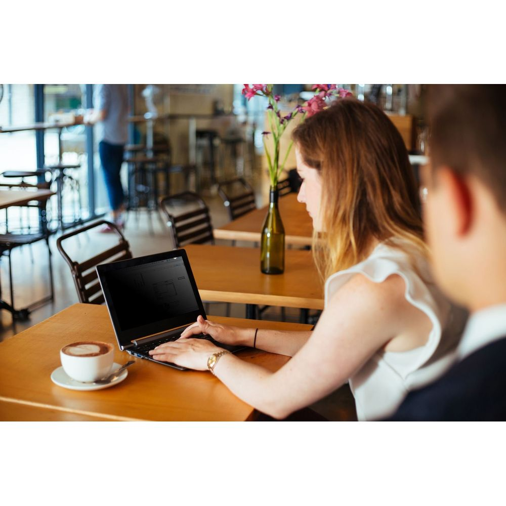 Mujer usando laptop en mesa de café con café y flores cerca.