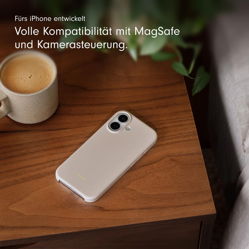 Una funda beige claro para iPhone reposa en una mesa de madera junto a una taza de café.