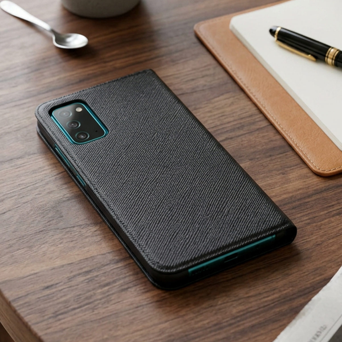 Telefono nero con fotocamera su scrivania in legno accanto a taccuino e penna.
