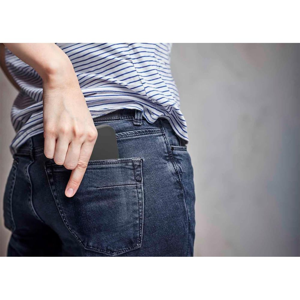 Una mano inserisce uno smartphone nero nella tasca posteriore di un jeans blu.