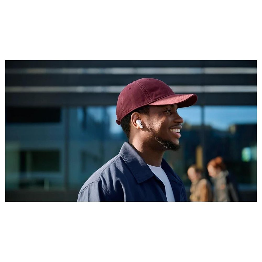 Mężczyzna w czapce i słuchawkach uśmiecha się przed nowoczesną architekturą.