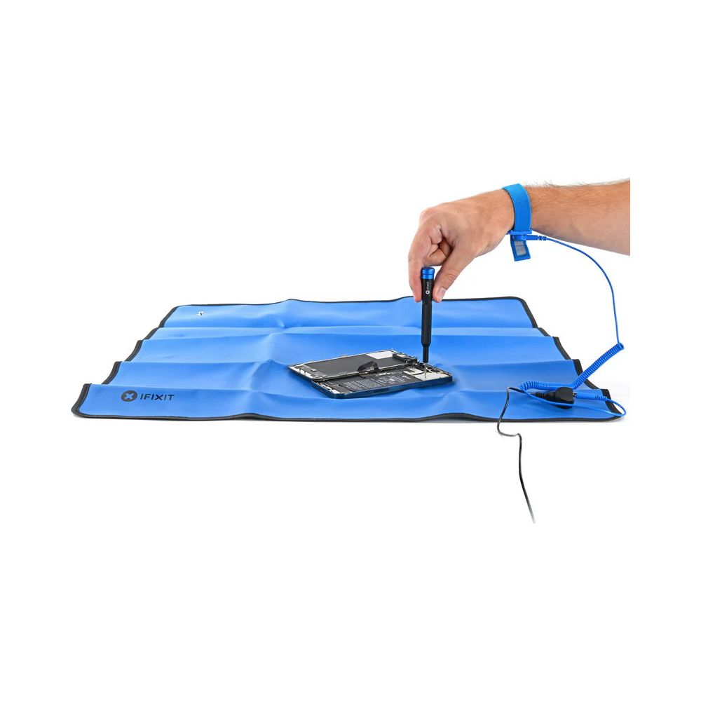 Mano con cacciavite ripara telefono su tappetino blu, con braccialetto antistatico.