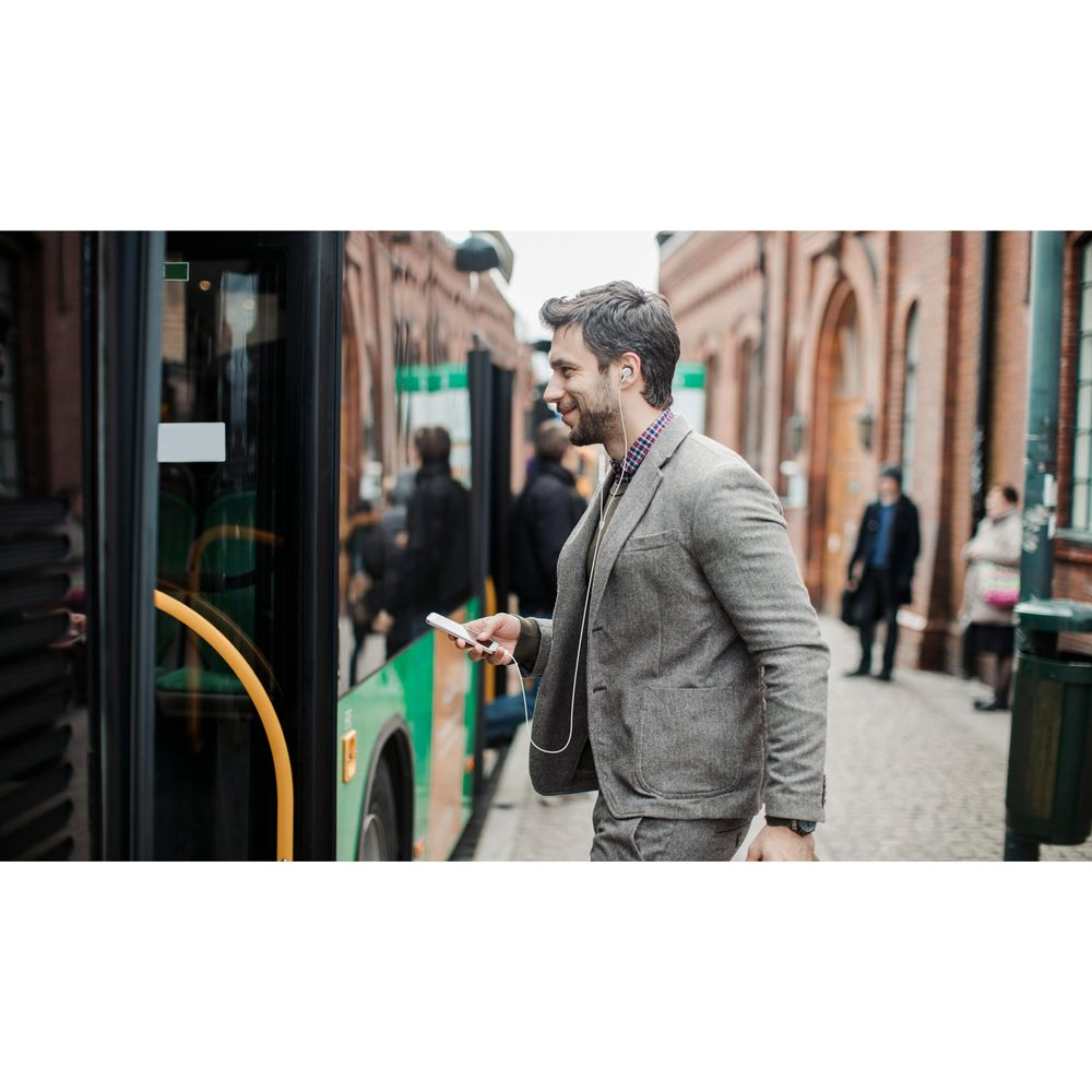 Mężczyzna w garniturze wsiada do zielonego autobusu, trzymając telefon.