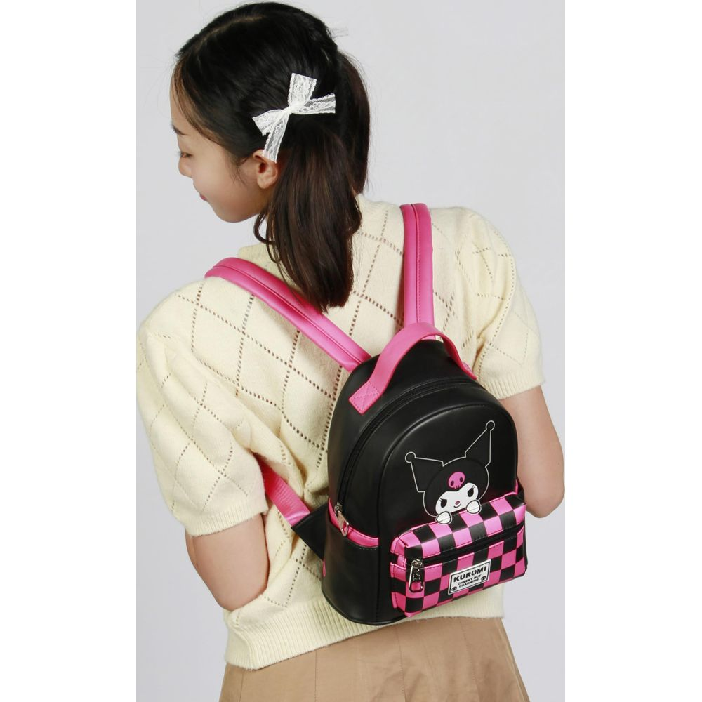 Ein Mädchen mit einem gelben Pullover trägt einen kleinen schwarzen Rucksack mit Kuromi-Motiv.